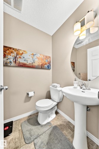 Powder room featuring a pedestal sink, round mirror, and tile flooring - 875 Chappelle Link Link, Edmonton, AB 