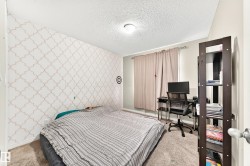 Carpeted bedroom featuring patterned accent wall, neutral wall paint, and a window with curtains - 