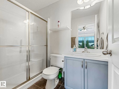 Shower enclosure with sliding glass doors, white vanity with light blue cabinetry, integrated sink, and wall-mounted mirror - 62 3075 Trelle Crescent Nw, Edmonton, AB - Indoor Photo Showing Bathroom