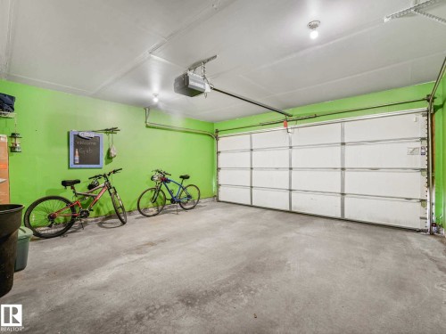 Spacious garage featuring a concrete floor, a white sectional garage door, a ceiling-mounted garage door opener, and bright green walls - 62 3075 Trelle Crescent Nw, Edmonton, AB - Indoor Photo Showing Garage