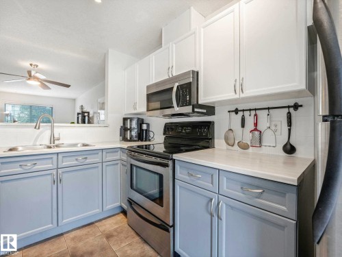 Kitchen featuring white upper cabinetry, light blue lower cabinetry, stainless steel appliances, a double basin sink, and a white countertop - 62 3075 Trelle Crescent Nw, Edmonton, AB - Indoor Photo Showing Kitchen With Double Sink