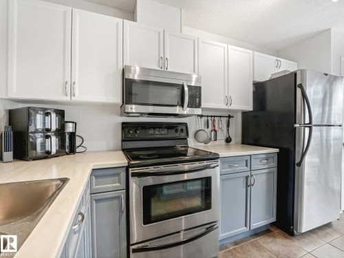 Kitchen featuring stainless steel appliances, white upper cabinetry, and contrasting grey lower cabinetry - 62 3075 Trelle Crescent Nw, Edmonton, AB - Indoor Photo Showing Kitchen