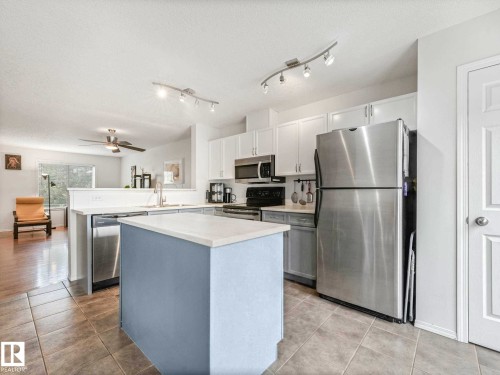 Kitchen featuring a center island with a light-colored countertop, white upper cabinetry, stainless steel appliances, and track lighting - 62 3075 Trelle Crescent Nw, Edmonton, AB - Indoor Photo Showing Kitchen