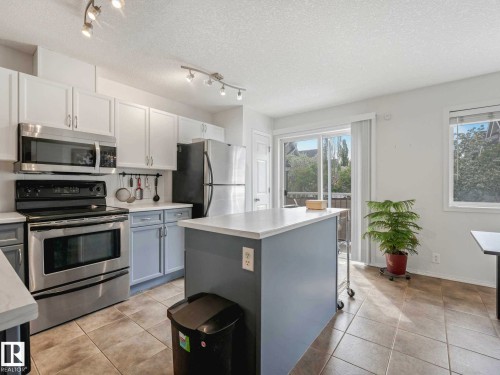 Kitchen featuring stainless steel appliances, upper white cabinetry, lower grey cabinetry, a center island with a white countertop, and tile flooring - 62 3075 Trelle Crescent Nw, Edmonton, AB - Indoor Photo Showing Kitchen