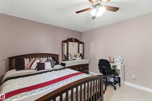 Carpeted bedroom featuring a ceiling fan with integrated lighting, neutral wall tones, and white baseboards - 4428 11A Avenue, Edmonton, AB 