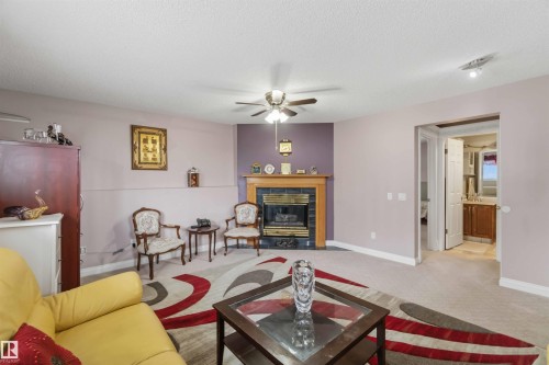 Living area with a ceiling fan, light-colored carpet, and a fireplace featuring a black tile surround and wood mantel - 4428 11A Avenue, Edmonton, AB 