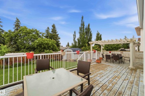 Expansive outdoor deck featuring a decorative pergola, white railing, and a private backyard with mature trees - 4428 11A Avenue, Edmonton, AB 