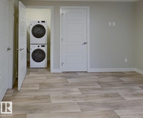 Dedicated laundry area featuring a stacked washer and dryer, complemented by wood-finish flooring and multiple paneled doors throughout - #Basement 10923 159 St Nw, Edmonton, AB - Indoor Photo Showing Other Room