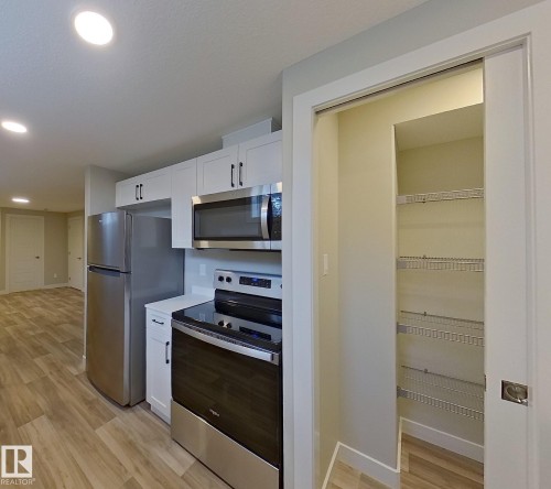 Modern kitchen featuring stainless steel appliances, white cabinetry with dark hardware, solid surface countertops, and wood-finish flooring - #Basement 10923 159 St Nw, Edmonton, AB - Indoor Photo Showing Kitchen