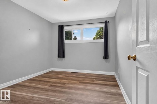 Room featuring light gray walls, wood-finish flooring, white baseboards, and a window with black curtain rods - 13431 109 Street, Edmonton, AB 