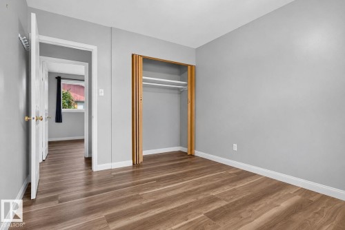 Bedroom featuring wood-finish flooring, light grey walls, white trim, and an open closet with bi-fold doors - 13431 109 Street, Edmonton, AB 
