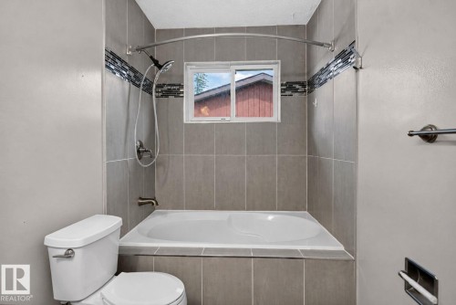 Built-in bathtub with neutral-toned rectangular tile surround and a decorative mosaic tile accent band - 13431 109 Street, Edmonton, AB 
