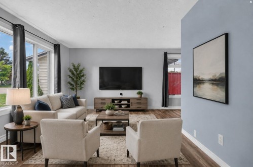 Spacious living area featuring large windows, wood-finish flooring, light blue wall paint, and white baseboards - 13431 109 Street, Edmonton, AB 