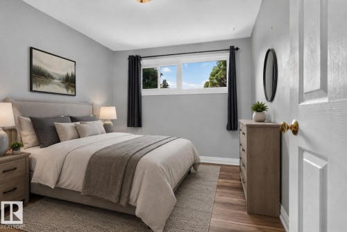 Bedroom featuring light gray walls, wood-finish flooring, a multi-pane window with dark drapery, a ceiling-mounted light fixture, and a paneled white door with a brass knob - 13431 109 Street, Edmonton, AB 