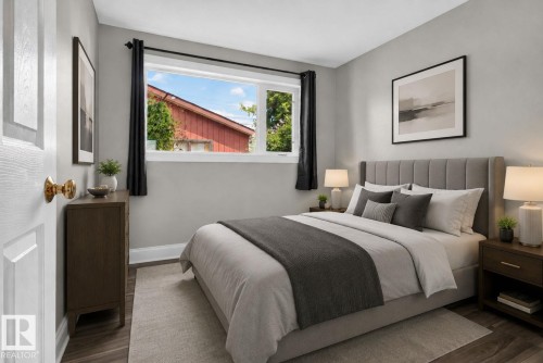 Bedroom featuring a large window, light gray walls, dark wood-finish flooring, white trim, and a panel-style door with a brass knob - 13431 109 Street, Edmonton, AB 