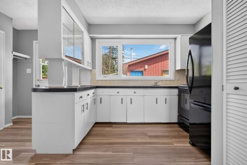 Kitchen featuring white cabinetry, dark countertops, wood-finish flooring, and a large window above the sink - 13431 109 Street, Edmonton, AB 