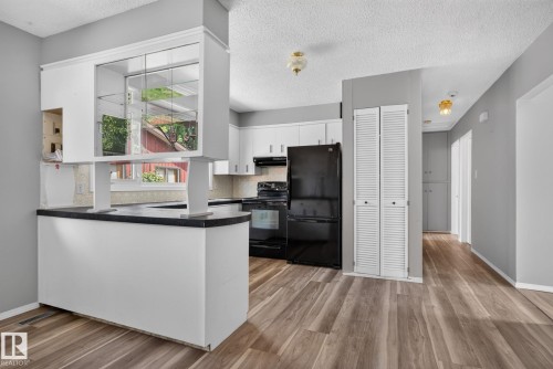 Kitchen featuring white cabinetry, black appliances, dark countertops, wood-finish flooring, and a pass-through window with display shelving - 13431 109 Street, Edmonton, AB 