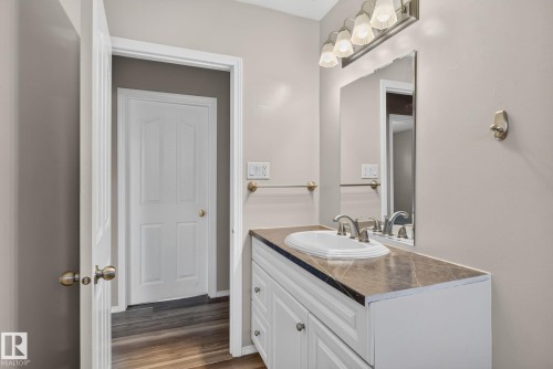 Bathroom featuring a white vanity with paneling, a dark countertop, an oval undermount sink with brushed nickel fixtures, a large mirror, and a four-light vanity fixture - 13431 109 Street, Edmonton, AB 