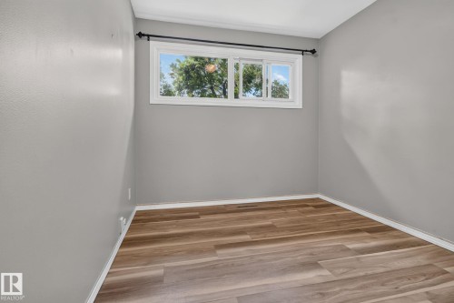 Room featuring wood-finish flooring, light gray wall paint, white baseboards, and a white-framed window - 13431 109 Street, Edmonton, AB 