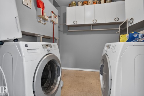 Dedicated laundry area featuring a front-load washing machine, built-in overhead cabinetry, open shelving, and neutral tone flooring - 13431 109 Street, Edmonton, AB 