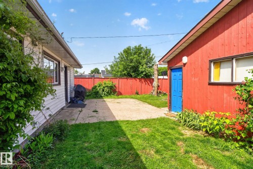 Spacious outdoor area featuring a concrete patio, green lawn, and a red privacy fence - 13431 109 Street, Edmonton, AB 