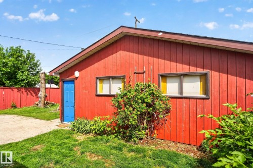 Red vertical siding exterior with a bright blue door, white trim, and a sloped roof - 13431 109 Street, Edmonton, AB 
