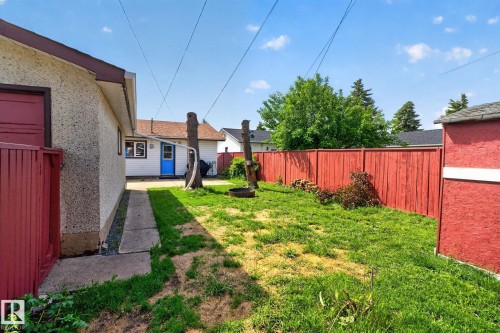Expansive backyard featuring a vibrant red privacy fence, a concrete walkway, and a detached building with a blue entry door - 13431 109 Street, Edmonton, AB 