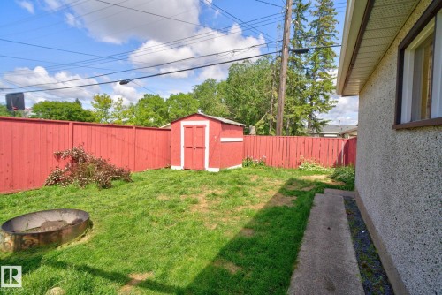 Grassed backyard featuring a red wood privacy fence, a red storage shed, a concrete walkway, and a fire pit - 13431 109 Street, Edmonton, AB 