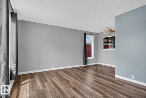 Spacious room featuring wood-finish flooring, light gray walls, white trim, and multiple windows providing natural illumination - 13431 109 Street, Edmonton, AB 