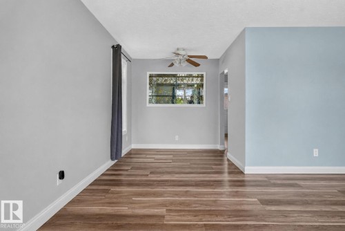 Spacious interior featuring wood-finish flooring, a ceiling fan, and a window with security bars - 13431 109 Street, Edmonton, AB 