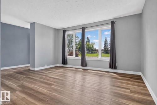 Spacious room featuring wood-finish flooring, a large multi-pane window, and light grey walls with white trim - 13431 109 Street, Edmonton, AB 
