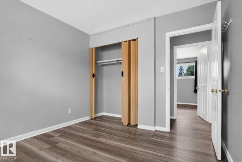 Interior room featuring wood-finish flooring, light gray walls, white baseboards, and a built-in closet with bi-fold doors - 13431 109 Street, Edmonton, AB 