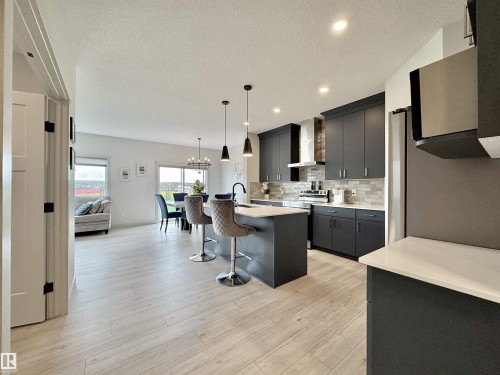 Open-concept kitchen featuring dark cabinetry, stainless steel appliances, a center island with seating, a white countertop, and a tiled backsplash - 33 Sumac Close, Fort Saskatchewan, AB 