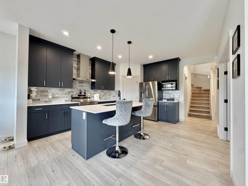 Modern kitchen featuring dark cabinetry with white countertops, a tiled backsplash, stainless steel appliances, and a central island with pendant lighting - 33 Sumac Close, Fort Saskatchewan, AB 