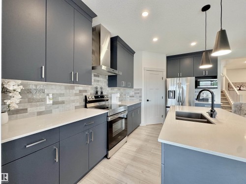 Kitchen featuring dark gray cabinetry with brushed nickel hardware, light wood-finish flooring, white countertops, and a subway tile backsplash - 33 Sumac Close, Fort Saskatchewan, AB 