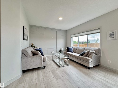Living area featuring a large window, light-toned wood-finish flooring, recessed lighting, and a detailed wainscoting accent wall - 33 Sumac Close, Fort Saskatchewan, AB 