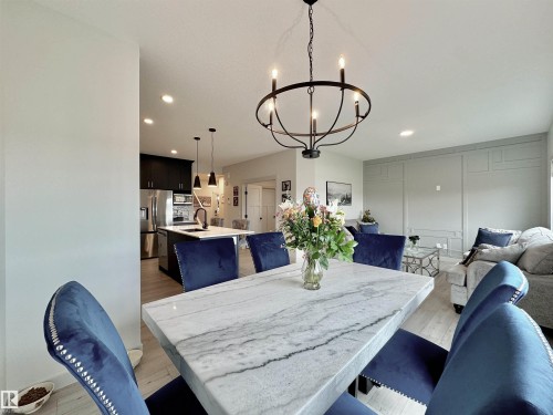 Open-concept dining area featuring a circular chandelier, light wood-finish flooring, and a marble-finish dining table - 33 Sumac Close, Fort Saskatchewan, AB 