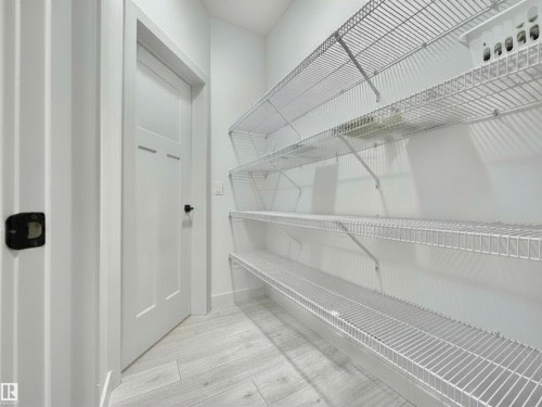 Utility room featuring white wire shelving, a multi-panel interior door with matte black hardware, and light wood-finish flooring - 33 Sumac Close, Fort Saskatchewan, AB 