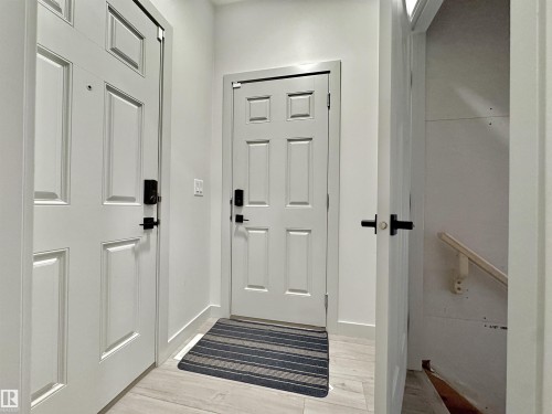 Entryway featuring three paneled doors with matte black hardware, light-toned wood-finish flooring, and crisp white baseboards - 33 Sumac Close, Fort Saskatchewan, AB 