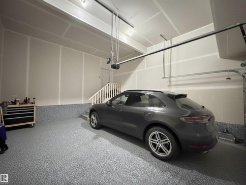 Spacious garage featuring a durable epoxy speckled floor, drywall-finished walls and ceiling, and a built-in staircase with a white railing - 33 Sumac Close, Fort Saskatchewan, AB 