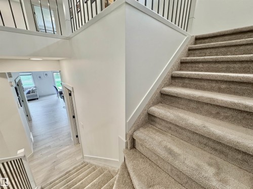 Split-level entry with carpeted stairs, white walls, and dark metal balusters - 33 Sumac Close, Fort Saskatchewan, AB 