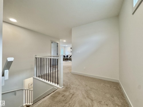 Upper-level landing featuring neutral-toned carpet, recessed lighting, and a white baluster railing with black spindles - 33 Sumac Close, Fort Saskatchewan, AB 