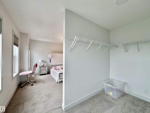 Carpeted interior space featuring white baseboards, multiple windows, and a walk-in closet with wire shelving - 33 Sumac Close, Fort Saskatchewan, AB 