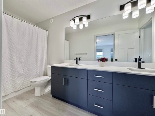 Bathroom featuring a dual vanity with a dark blue cabinet base, white countertops, and black fixtures - 33 Sumac Close, Fort Saskatchewan, AB 