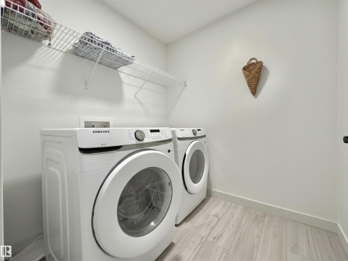 Dedicated laundry area featuring a front-loading washer and dryer, light wood-finish flooring, and wall-mounted wire shelving for storage - 33 Sumac Close, Fort Saskatchewan, AB 