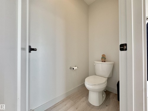 Powder room featuring a white toilet, light-colored walls, and wood-finish flooring - 33 Sumac Close, Fort Saskatchewan, AB 