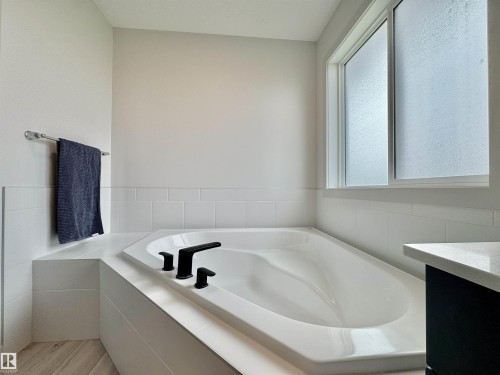 Corner soaking tub with black fixtures, surrounded by white subway tile wainscoting - 33 Sumac Close, Fort Saskatchewan, AB 