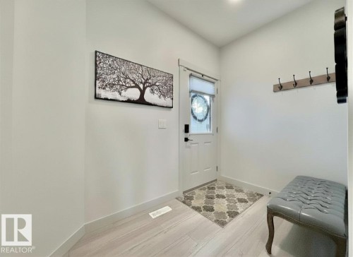 Foyer featuring light-toned wood-finish flooring, white trim, a white entry door with decorative glass, and a flush-mount ceiling light - 33 Sumac Close, Fort Saskatchewan, AB 