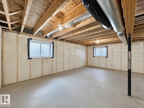 Unfinished basement with exposed ceiling joists, concrete flooring, insulated walls, two windows, and visible ductwork - 33 Sumac Close, Fort Saskatchewan, AB 