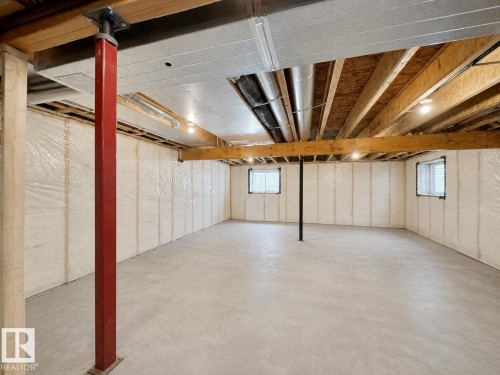 Spacious unfinished basement featuring a concrete floor, insulated walls with plastic sheeting, exposed wood ceiling joists, and two small windows - 33 Sumac Close, Fort Saskatchewan, AB 